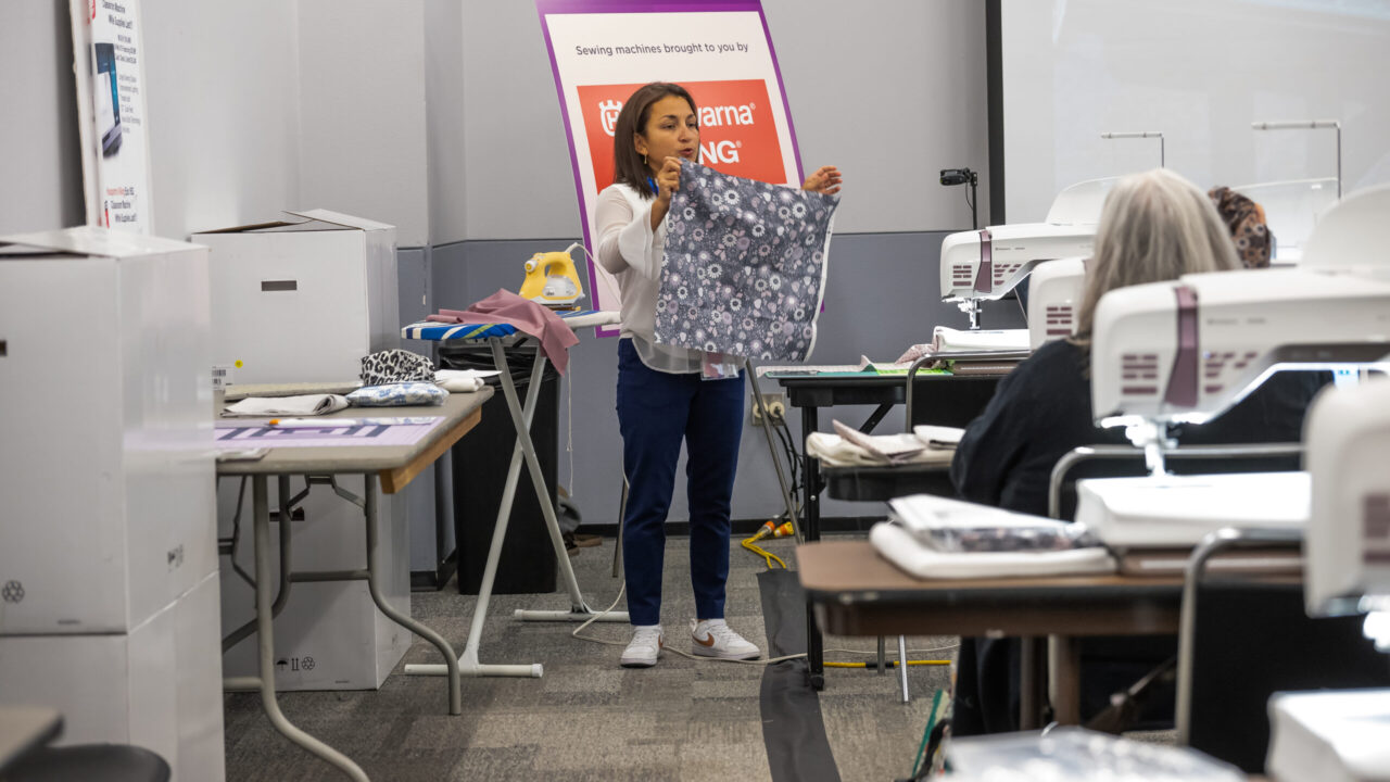 Instructor holding quilt in front of sit and sew classroom