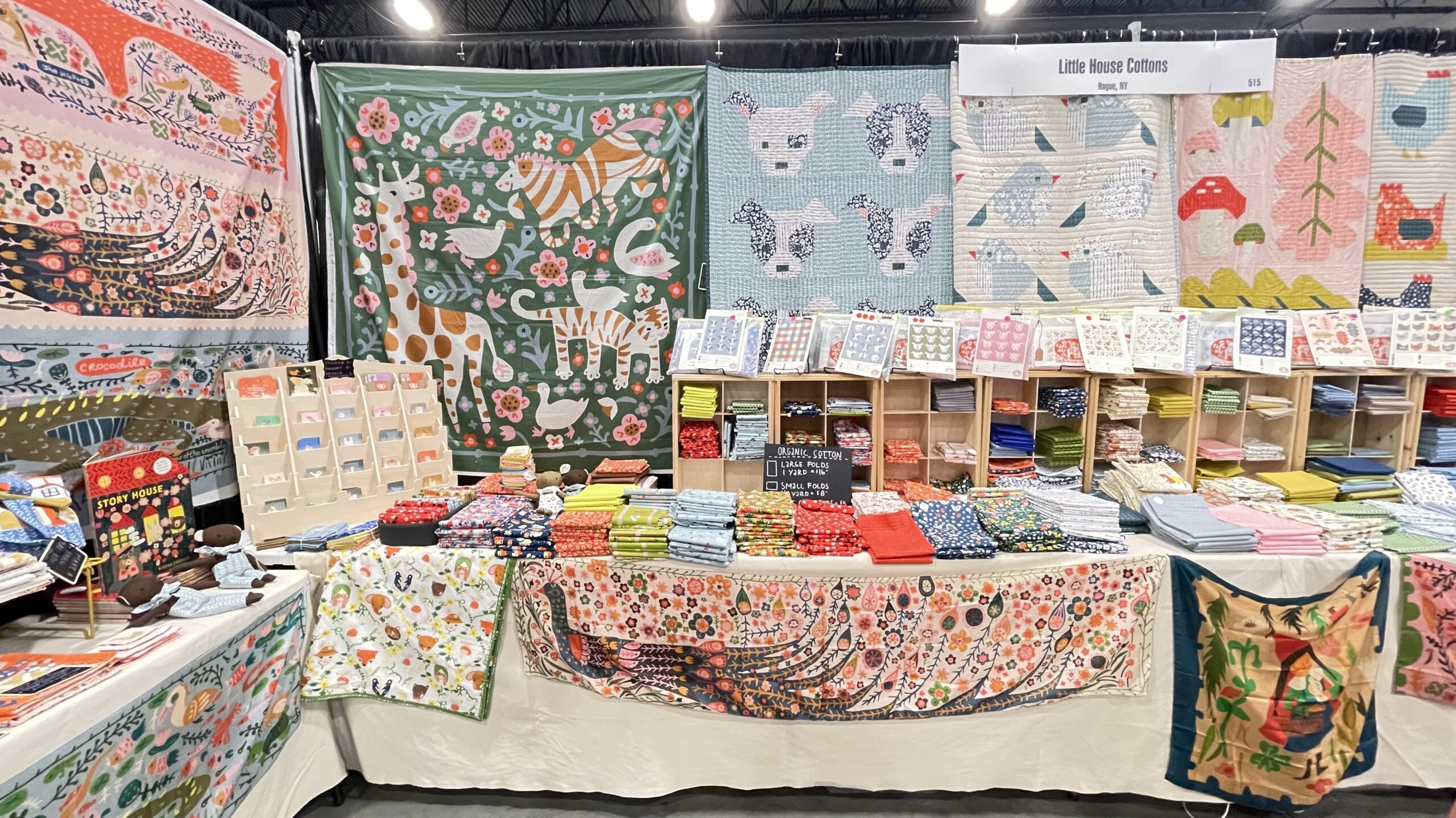 Little House Cottons booth layout with a variety of pastel colored quilts, fabrics, and notions