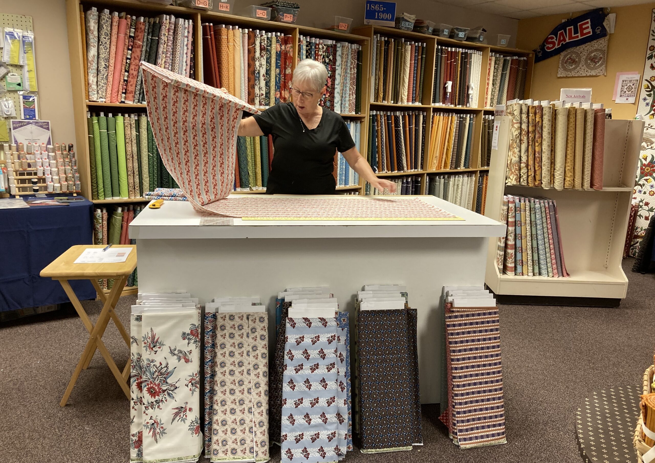 Bolts of fabric on shelves with shop owner working to cut fabric
